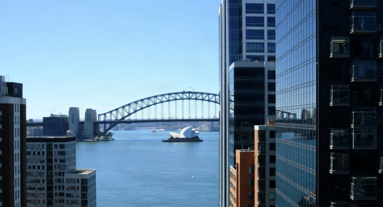 Sydney skyline with Harbour Bridge and Opera House under clear blue sky, representing Australia's economic landscape.