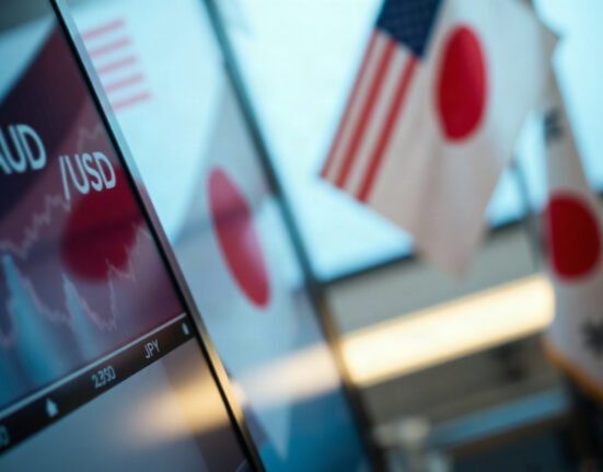 Currency trading screen showing AUD/USD and JPY pairs, with US and Japanese flags in background