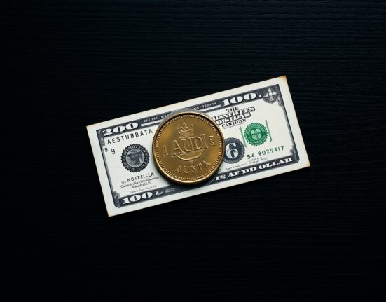 Australian Dollar coin and US Dollar bill on a dark wooden surface, representing forex market analysis.