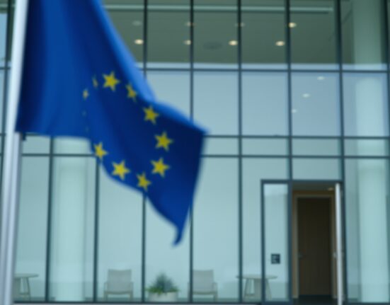 Exterior of a European Union regulatory building with a blurred EU flag in the foreground, representing crypto regulation.