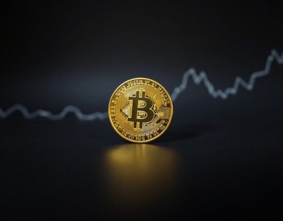 Bitcoin coin on a dark surface with a faint downward-trending graph in the background, representing a market bottom prediction.