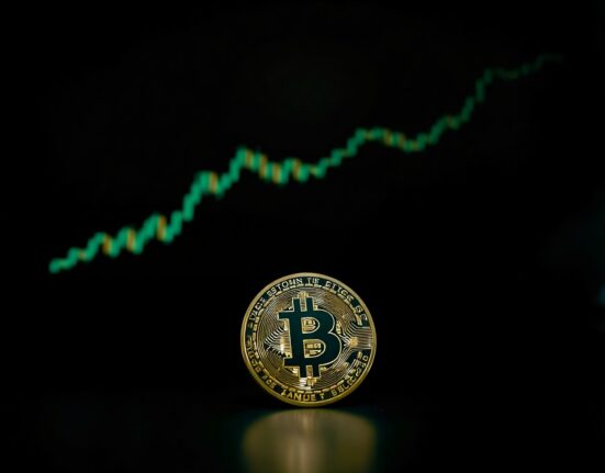 Bitcoin coin on a dark trading desk with a green chart in the background, representing a potential bullish market reversal.