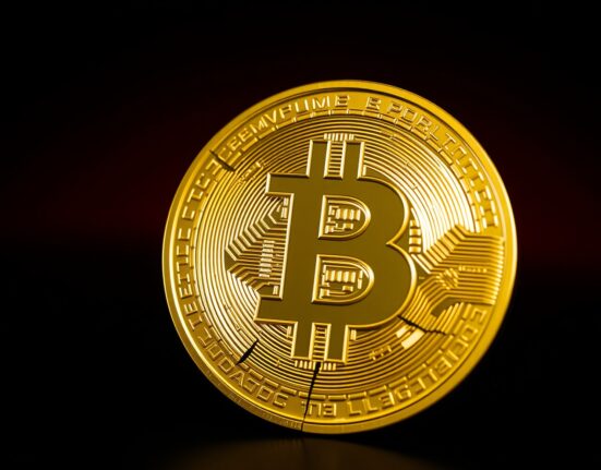 Fragmented Bitcoin symbol against dark background with red lighting, representing market volatility and liquidation risk.