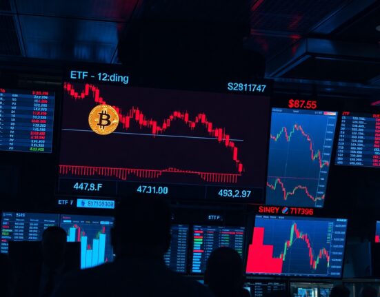 Trading floor monitors showing Bitcoin price charts and ETF data with red downward trend.