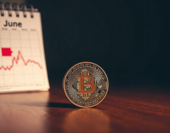 Bitcoin coin on a table with a June calendar and a downward trend graph in the background.
