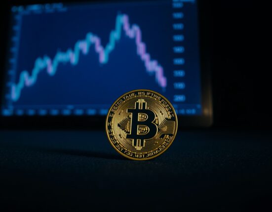 Bitcoin coin on dark surface with a downward-trending financial chart in the background, representing market correction risk.