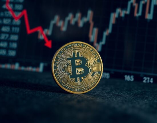 Bitcoin coin on dark surface with red shadow indicating financial pressure
