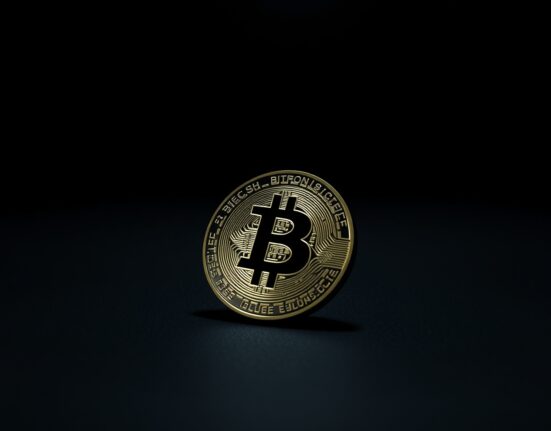 Bitcoin coin on dark surface with subtle red reflection indicating price decline