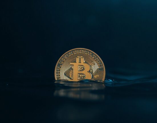 Bitcoin coin partially submerged in dark water, representing financial stress and potential market capitulation.