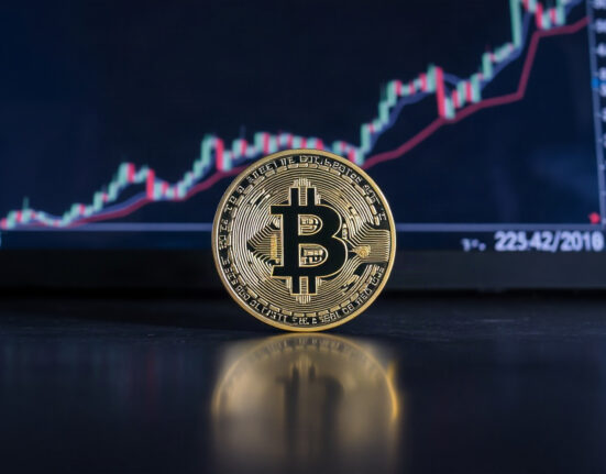 Bitcoin coin on reflective surface with a blurred upward chart in the background, symbolizing a price rally.