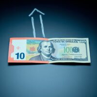 Canadian and US dollar banknotes on a desk with a downward trend graph, representing the weakening Canadian dollar due to BoC-Fed policy divergence.