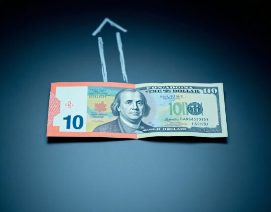 Canadian and US dollar banknotes on a desk with a downward trend graph, representing the weakening Canadian dollar due to BoC-Fed policy divergence.