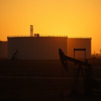 Oil pumpjack silhouette against sunset with storage tanks in background, representing Brent crude market pullback.