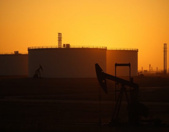 Oil pumpjack silhouette against sunset with storage tanks in background, representing Brent crude market pullback.