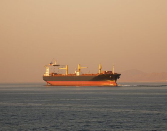 Oil tanker navigating the Strait of Hormuz under a hazy sunset, illustrating geopolitical supply risk.