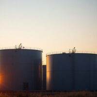 Oil storage tanks at sunset with refinery in background, representing Brent crude oil market analysis.