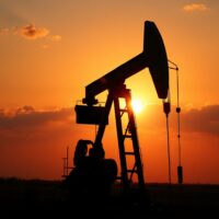 Oil pumpjack silhouette at sunset with a subtle map overlay, symbolizing geopolitical oil market risks.