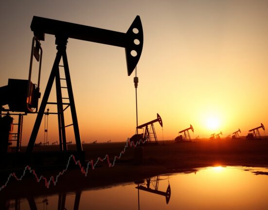 Oil pumpjack in field with Brent crude price chart reflection at sunset