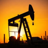 Crude oil pumpjack at sunset with refinery in background, representing supply risks.