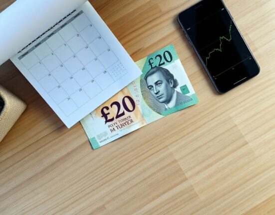 British Pound banknote on desk with calendar and smartphone showing chart ahead of UK GDP data release