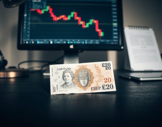 British Pound Sterling banknote on desk with GBP/USD chart on computer monitor in background
