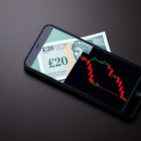 British pound banknote and smartphone showing forex chart representing currency volatility and analysis.