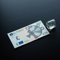 British Pound banknote and oil barrel figurine on desk representing currency and energy market dynamics
