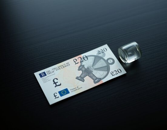 British Pound banknote and oil barrel figurine on desk representing currency and energy market dynamics