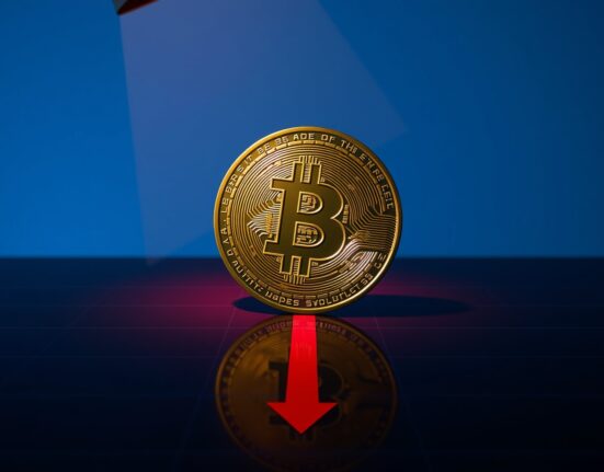 Bitcoin coin with red downward shadow representing BTC falls below $77,000 price crash