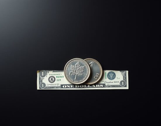 Canadian loonie coin and US dollar bill on a desk representing USD/CAD forex consolidation.