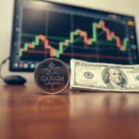 Canadian loonie coin and US dollar bill on desk with forex chart in background