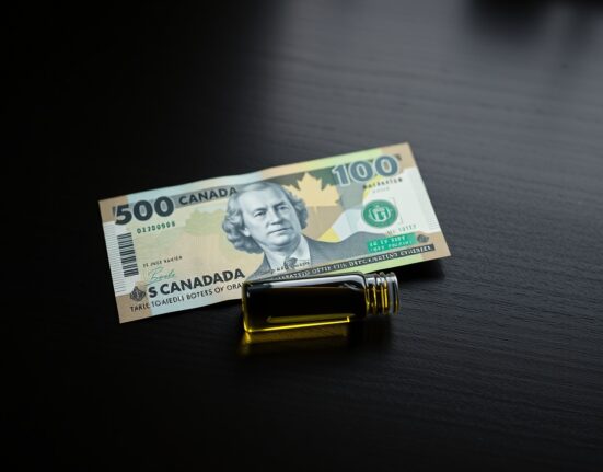Canadian dollar banknote beside a vial of crude oil on a wooden surface, representing currency and commodity market dynamics.