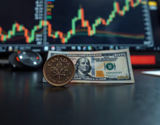 Canadian loonie coin and U.S. dollar bill on a financial desk with a chart in the background