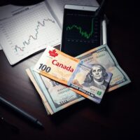 Canadian and US dollar bills on a desk with a forex chart in the background