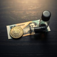 Canadian loonie coin and crude oil vial representing the correlation between the Canadian dollar and oil prices.