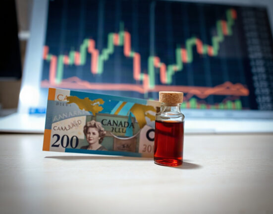 Canadian dollar banknote and oil vial on desk with financial charts in background
