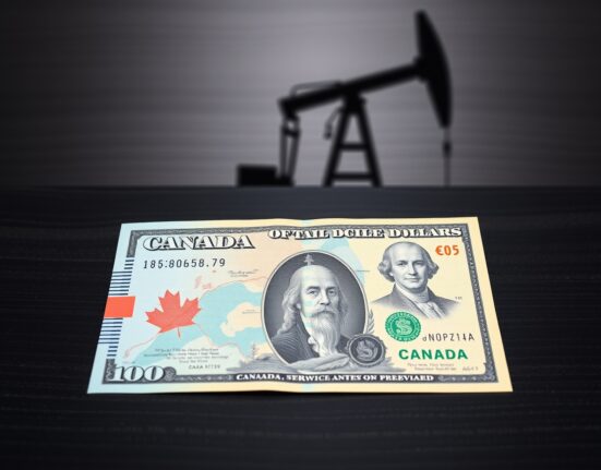 Canadian dollar and US dollar banknotes on a dark surface with a blurred oil derrick in the background.
