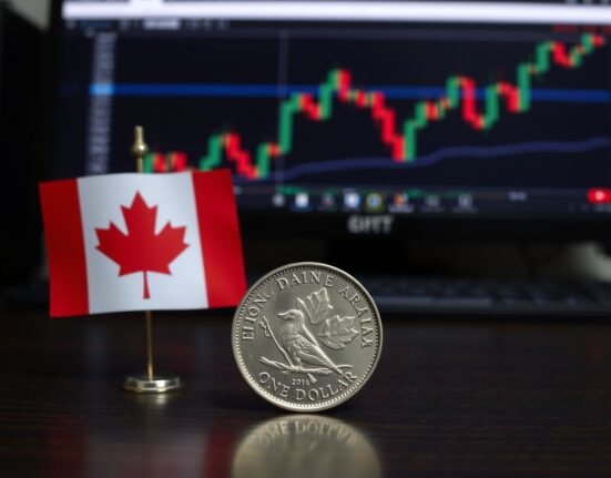 Canadian Loonie coin on a desk with a flag and forex chart in the background