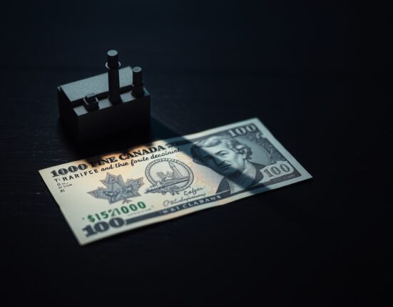 Canadian dollar banknote with a shadow of a factory model representing tariffs