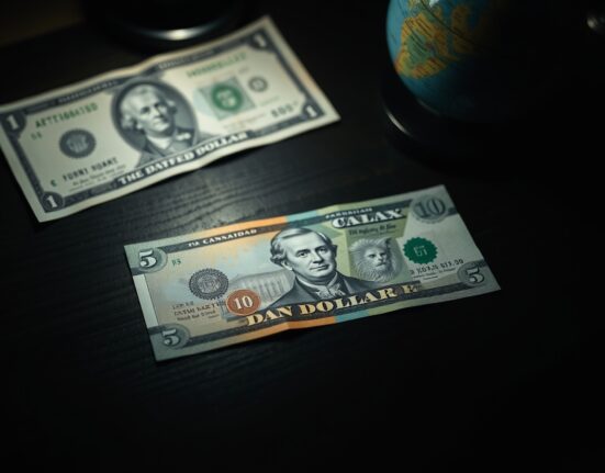 Canadian dollar banknote on desk with globe and US dollar in background, representing forex market pressure
