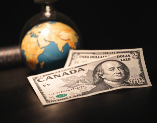 Canadian and US dollar banknotes on a desk with a blurred globe in the background, representing currency market volatility due to geopolitical tensions.