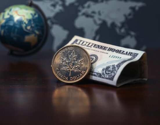 Canadian loonie and US dollar bill on a dark surface, representing forex market dynamics.
