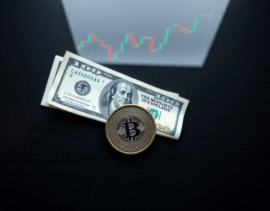 Canadian dollar coin and US dollar bill on wooden surface with stock chart reflection