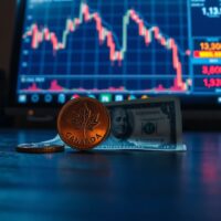Canadian loonie coin and US dollar bill on desk with financial chart in background