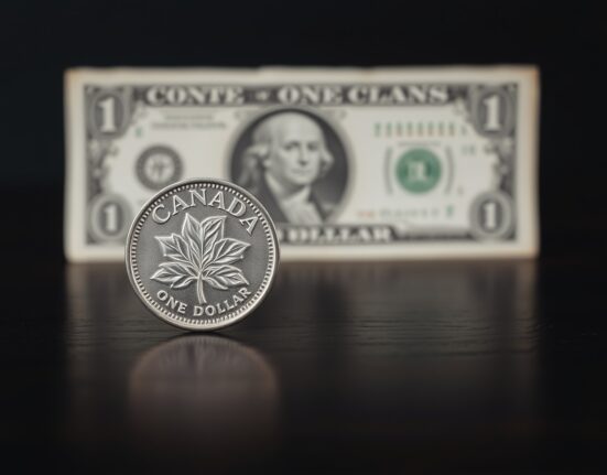 Canadian loonie coin and US dollar bill on a dark surface, representing currency exchange rate weakness.