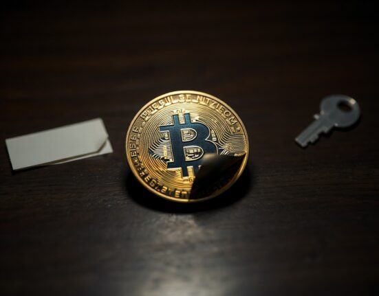 A Casascius physical Bitcoin coin with hologram partially peeled, on a wooden surface.