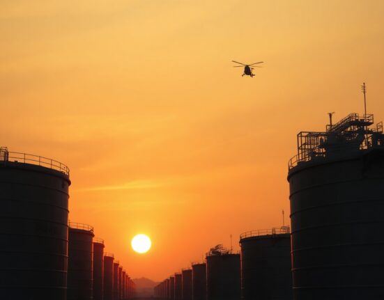 Crude oil storage tanks at sunset with a military helicopter silhouette in the distance.