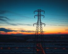 Aerial view of a large data center campus near power transmission lines at dusk, illustrating grid connectivity challenges.