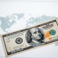 US dollar banknote in focus with blurred world map background, representing safe-haven demand amid geopolitical uncertainty.