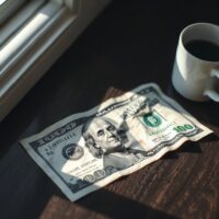 US dollar banknote on wooden table with coffee cup, representing currency market awaiting CPI data